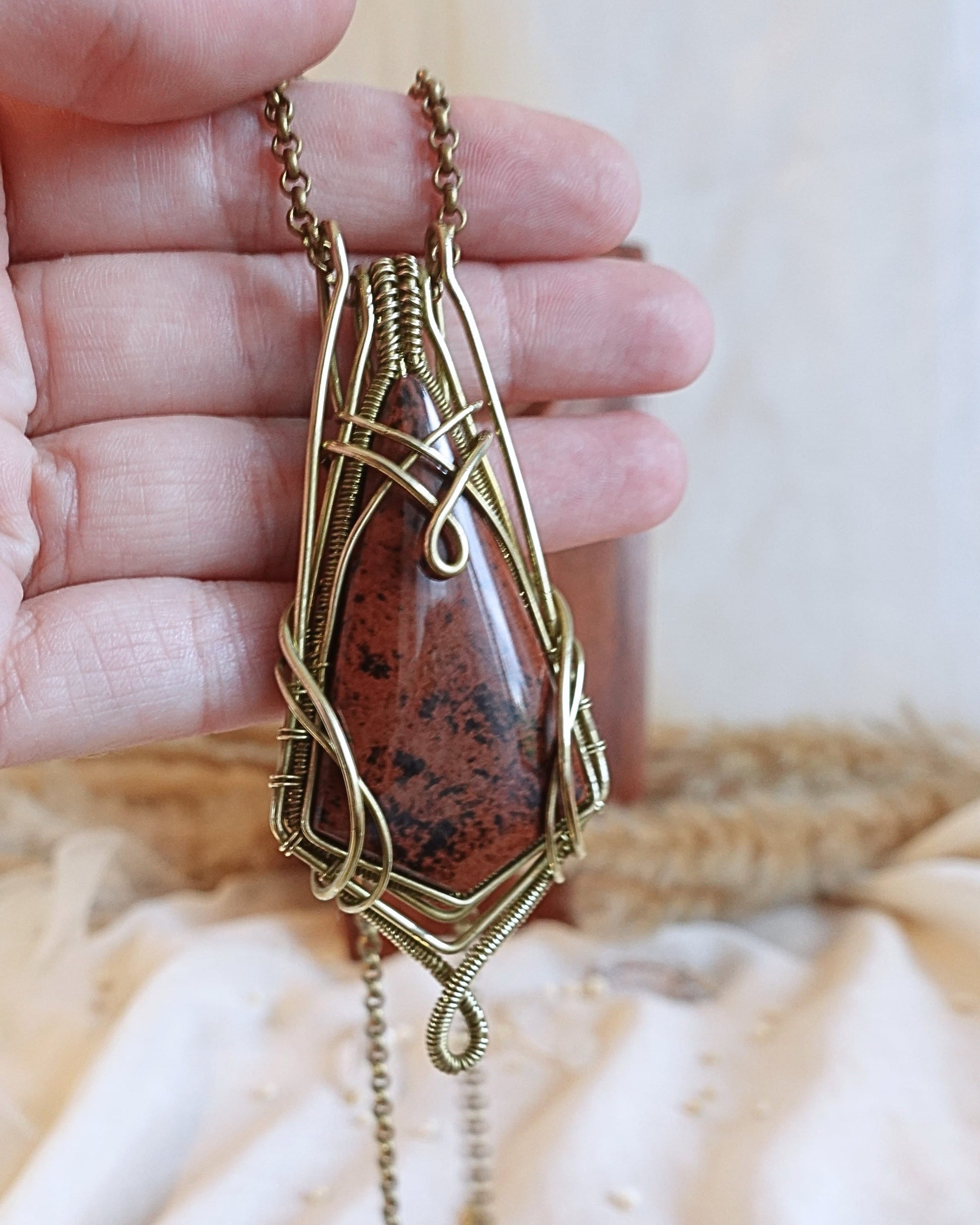 Side view of mahogany obsidian wirewrap pendant on brass chain